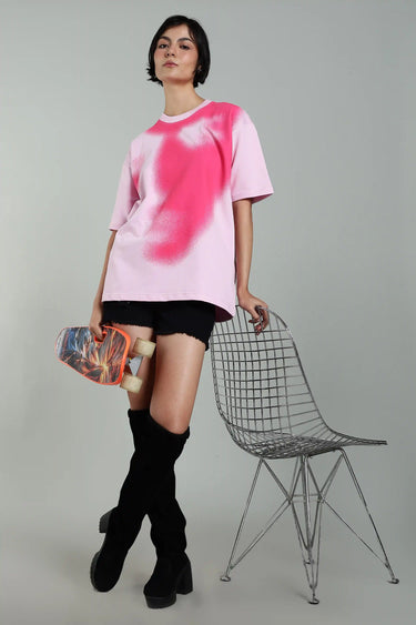 A woman posing with a skateboard and chair while wearing the pink abstract face t-shirt