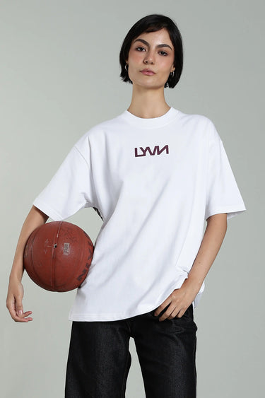 A woman wearing the oversized, unisex white phoenix t-shirt with the LYVN logo on the front, holding a basketball against a plain background