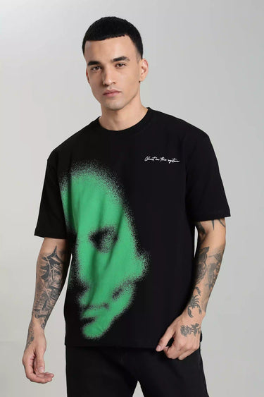 A man wearing a black t-shirt with a green abstract face on a plain background