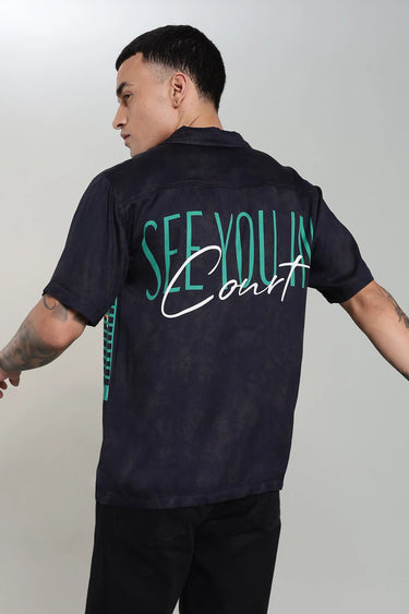 A man wearing a navy tennis print shirt with 'See You In Court' text on the back against a plain background