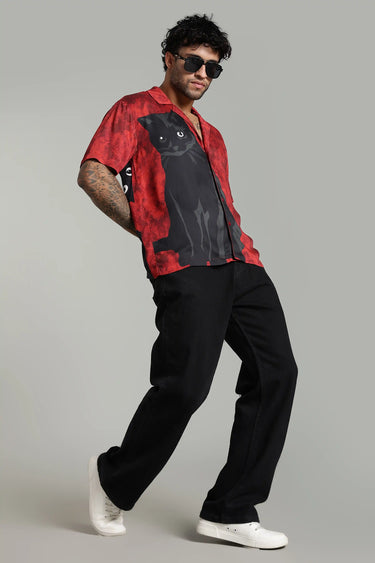 Man wearing a red shirt with a black cat design and black pants on a gray background