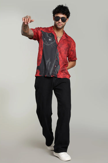 Man wearing a red shirt with a black cat design and black pants on a gray background