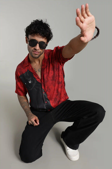 Man wearing a red and black cat shirt, sunglasses, and black pants on a gray background