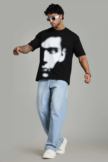 Man wearing a black oversized t-shirt with an abstract face design, styled with light blue jeans and sunglasses.
