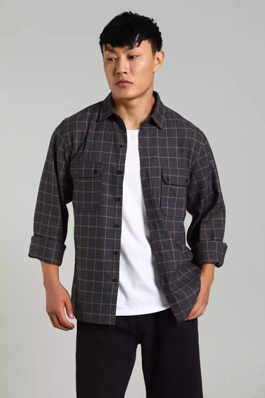 Man posing with a checked shacket over a white t-shirt on a gray background