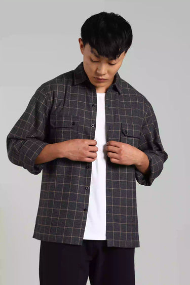 A man wearing a checked shacker over a white shirt on a plain background