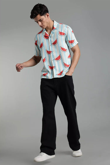 Man wearing a light blue shirt with watermelon pattern and black pants on a gray background