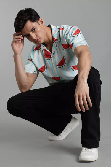 Man wearing a watermelon pattern shirt and black pants on a gray background