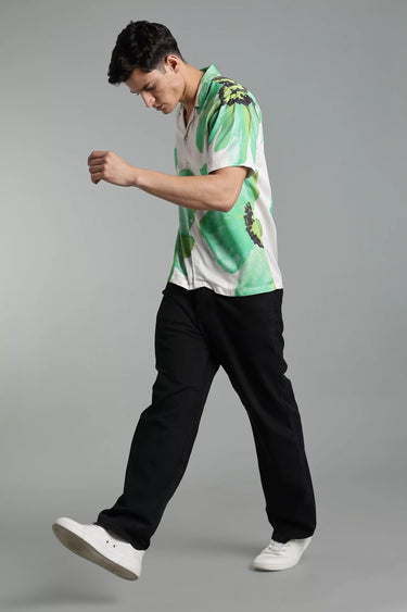 Man wearing a green and white floral printed shirt with black pants on a gray background
