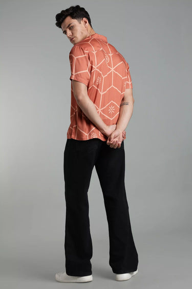 A man wearing a brown tile patterned shirt and black pants on a gray background