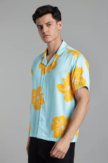 Side profile of a man wearing a light blue shirt with yellow floral patterns on a gray background