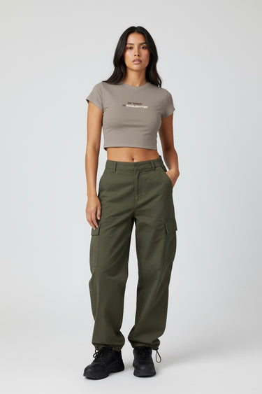 Woman wearing a dark beige crop top that says Ddon't Gaslight the Gaslighter' and cargo pants on a white background