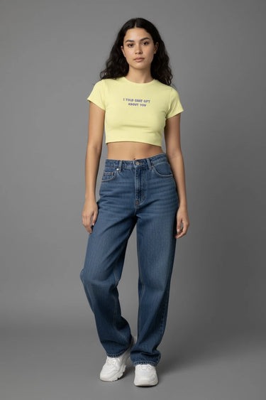 Woman wearing a yellow graphic crop top and blue jeans on a gray background