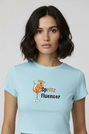 Woman wearing a light blue graphic crop top with 'Aperol Spritz fluencer' design on a plain background