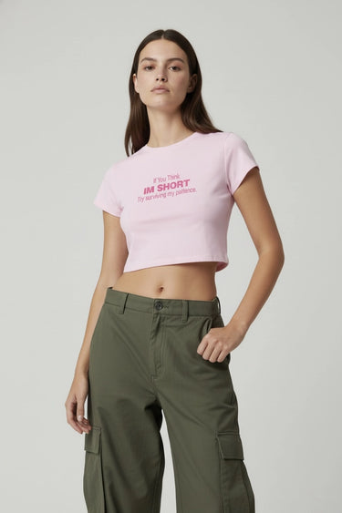 Woman wearing a pink graphic crop top with text and green cargo pants on a light gray background
