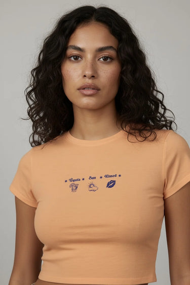Woman wearing an orange graphic crop top with small designs and text on a plain background
