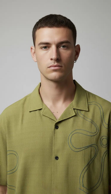 Man wearing a green relaxed fit embroidered shirt with abstract patterns against a plain background