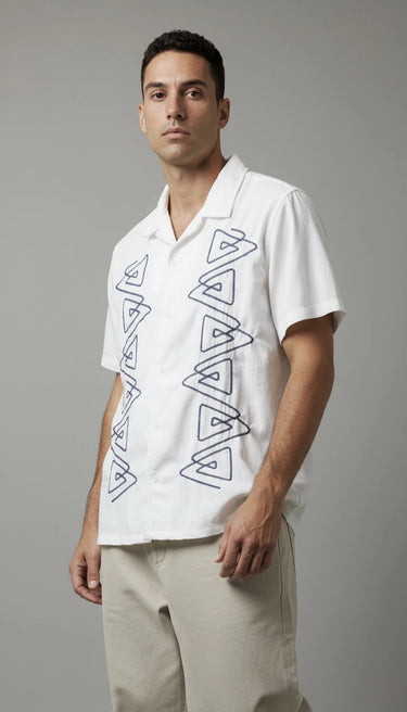 Man wearing a white shirt with embroidered geometric patterns on a gray background