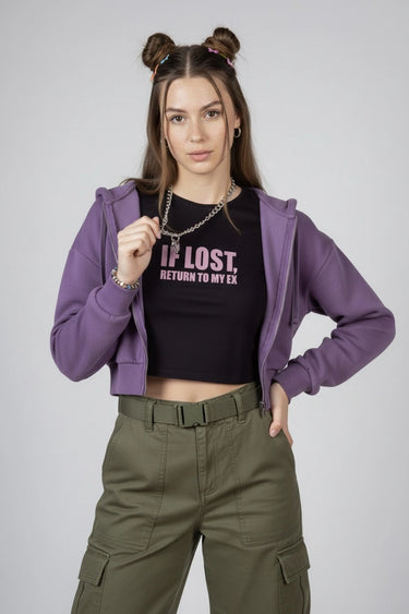 A woman wearing a purple hoodie, a black t-shirt with text that says "If Lost, Return to my Ex" and green cargo pants on a plain background