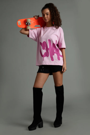 a woman wearing a pink chaotic oversized unisex t-shirt, holding a skateboard
