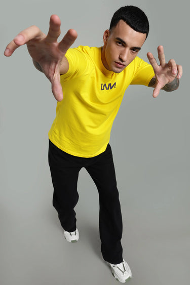 A man wearing the yellow caution oversized t-shirt with the LYVN logo, posing against a gray background