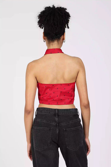 Backview of a woman wearing a red halter cropped shirt and black high-waisted jeans on a white background