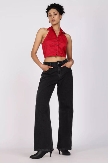 A woman wearing a red halter cropped shirt and black high-waisted jeans on a white background
