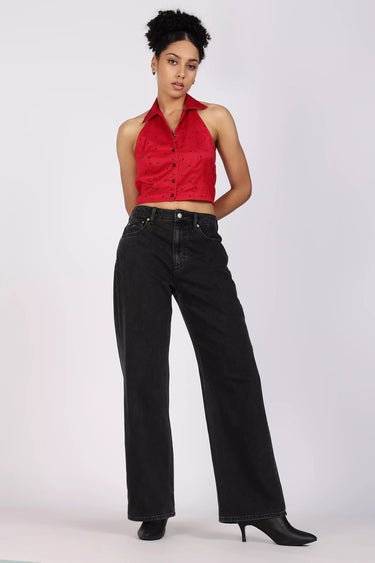 A woman posing with red halter croppped shirt and black high-waisted jeans on a white background