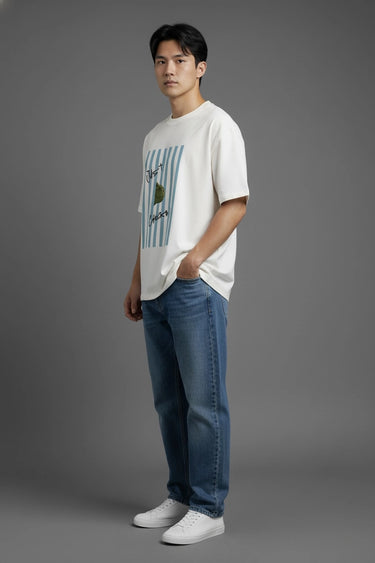 Man wearing half white unisex oversized  t-shirt with a graphic design and blue jeans on a gray background