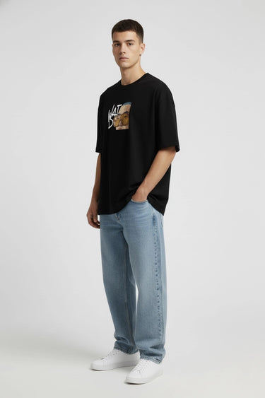 Black oversized graphic t-shirt with colorful "Whatcha' doing" design, paired with light blue jeans and white sneakers.