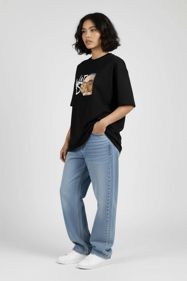 Black oversized graphic t-shirt with cartoon fox design, paired with light blue jeans and white sneakers.