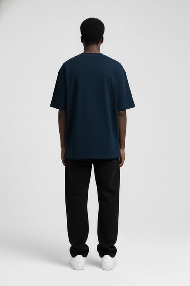 Man wearing navy oversized graphic t-shirt with relaxed fit, paired with black pants and white sneakers, back view.