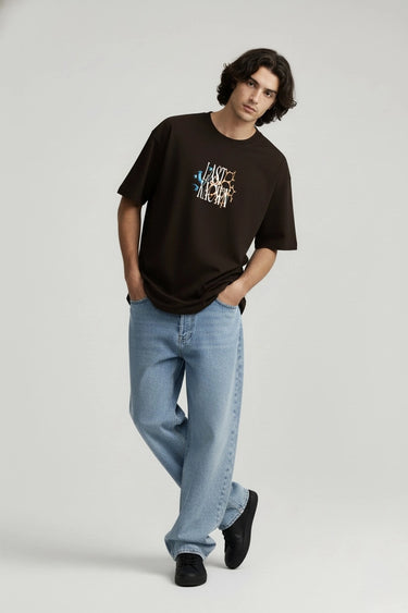 Black oversized graphic t-shirt with colorful "LAST KNOWN" text paired with light blue jeans and black shoes.