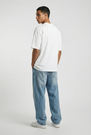 White oversized graphic t-shirt with relaxed fit on model wearing light blue jeans and white sneakers.