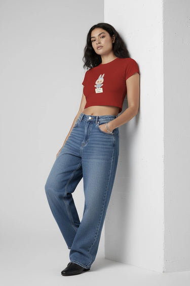 A woman posing with the red drama graphic crop top with blue jeans leaning against a wall. 