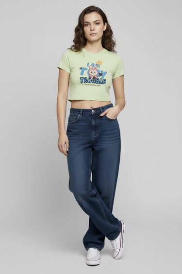 Light green graphic crop top with colorful monster print and short sleeves worn with dark blue jeans. - LYVN