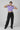 Person wearing a purple crop top with graphic designs and black jeans on a plain background
