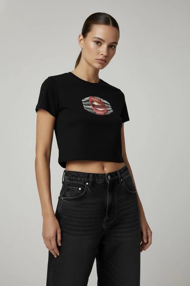 Woman wearing a black graphic crop top with a graphic design and black jeans on a gray background
