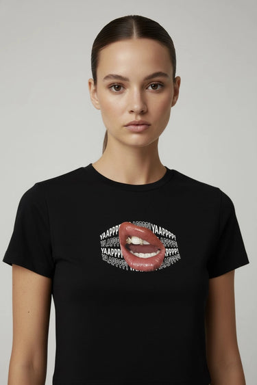 Person wearing a black graphic crop top with a graphic design of lips and text on a plain background