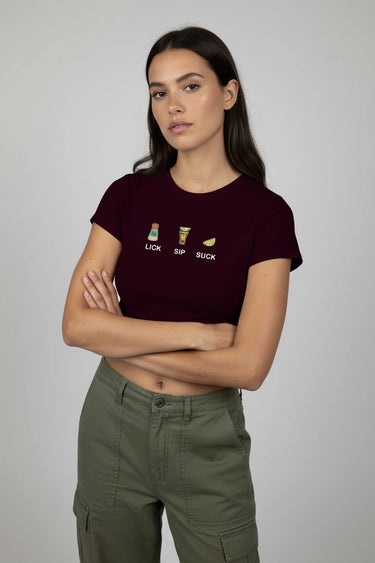 Woman wearing a maroon graphic crop top with text and green pants on a plain background