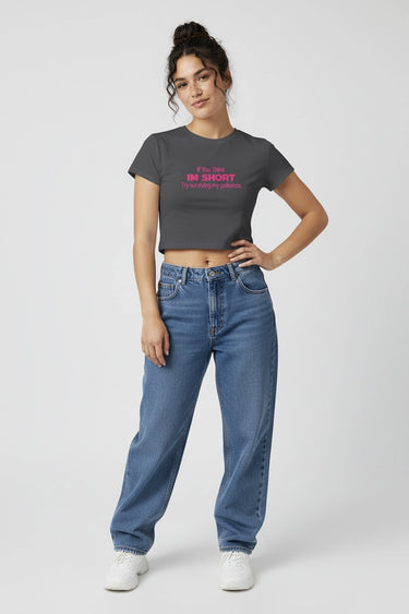 Woman wearing a dark gray graphic crop top with pink text and blue jeans on a white background
