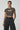Woman wearing a brown crop top with text 'If You Find Me Relatable Seek Help!' and black pants on a white background