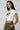 Woman wearing a white graphic crop top with a graphic design on a plain background