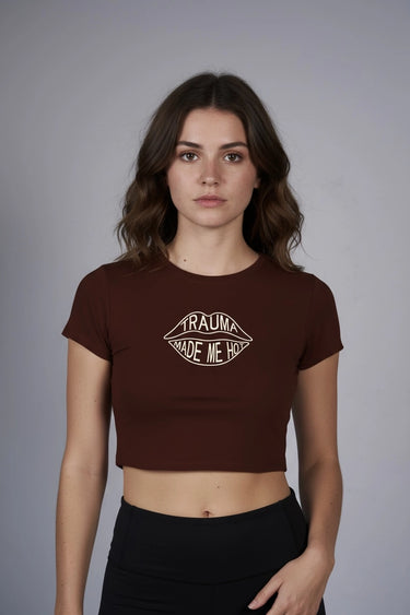 Woman wearing a brown graphic crop top with text that says "Trauma Made Me Hot" against a gray background