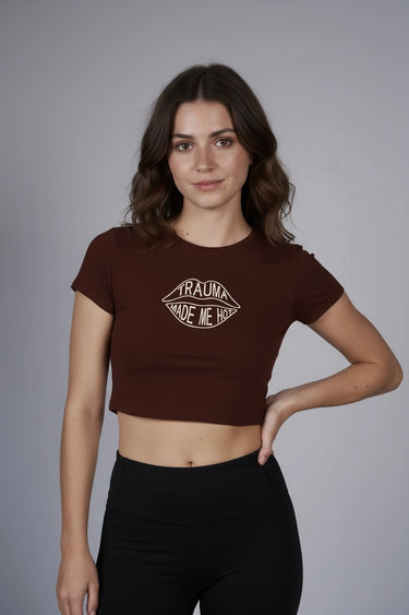 Woman wearing a brown graphic crop top with a graphic design that says "Trauma made me hot" on a gray background