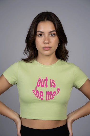 Woman wearing a green GRAPHIC crop top with pink text that says "is she me" against a gray background