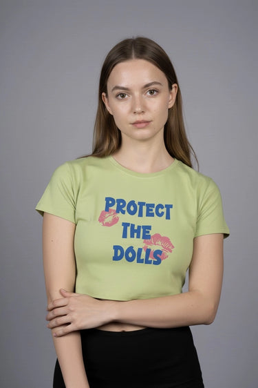 Person wearing a green graphic crop top with 'Protect the Dolls' text and on a gray background