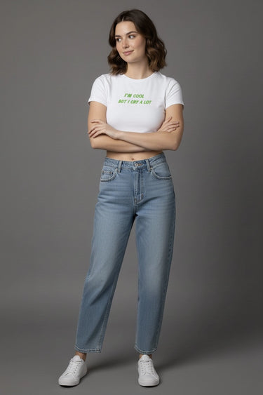 Woman wearing a white graphic crop top with text and blue jeans on a gray background