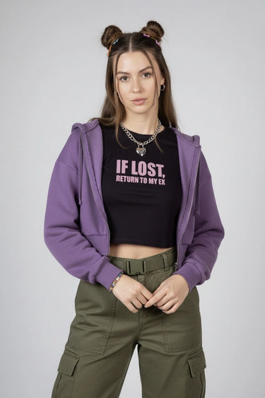 Woman wearing a purple hoodie, black graphic crop top with text, and green cargo pants on a plain background
