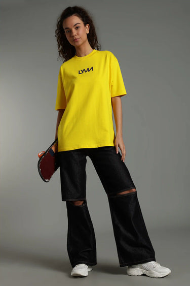A woman wearing the yellow caution oversized t-shirt with the LYVN brand logo on a gray background